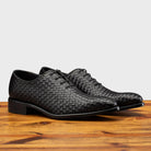 A Pair of Black woven dress shoe on a wooden surface with a light gray background