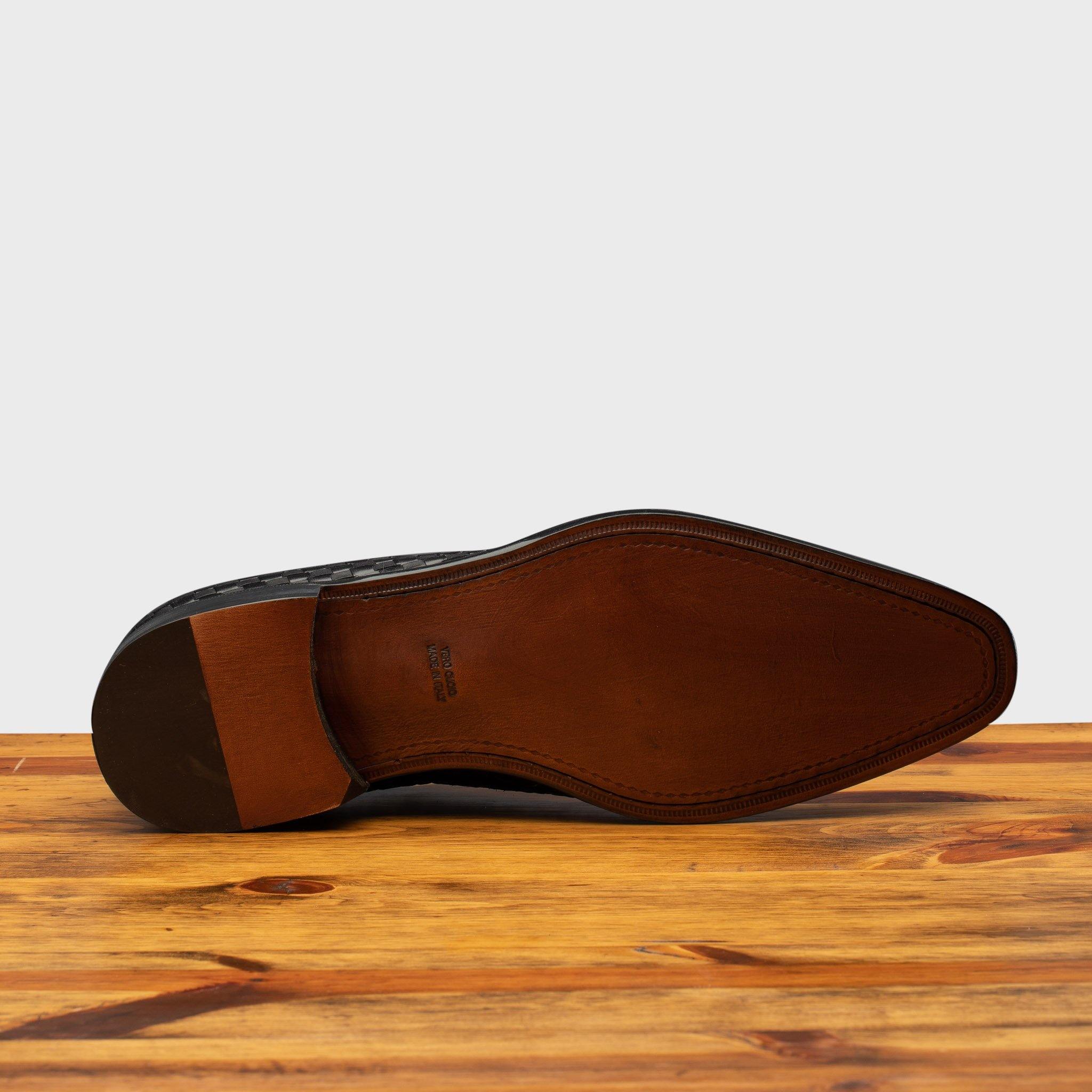 Outsole of Black woven dress shoe on a wooden surface with a light gray background