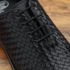 Black woven dress shoe on a wooden surface