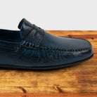 Blue leather loafer on a wooden surface with a white background