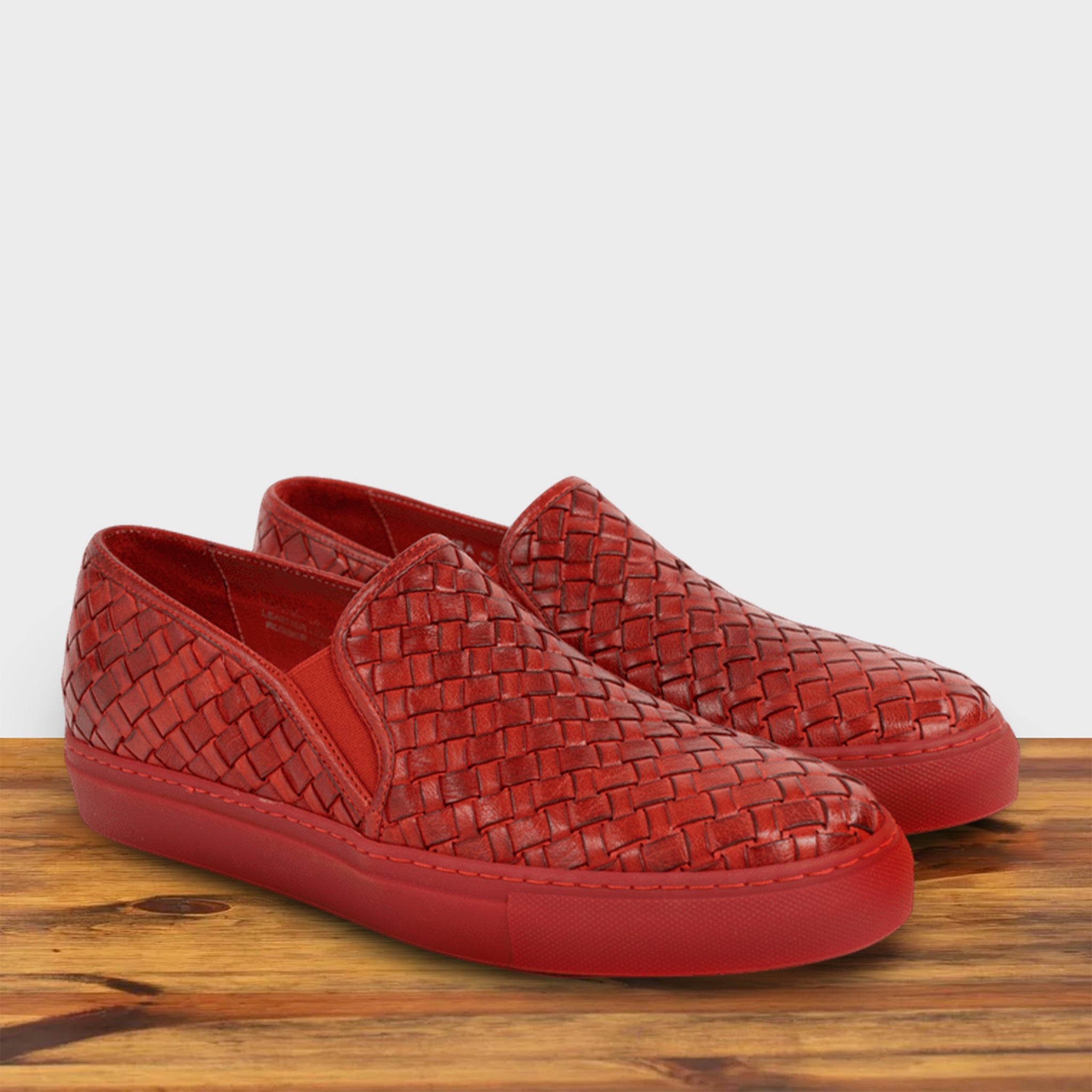 A Pair of Red woven slip-on shoe on a wooden surface with a white background