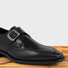 A black monk strap shoe with a silver buckle on a wooden surface