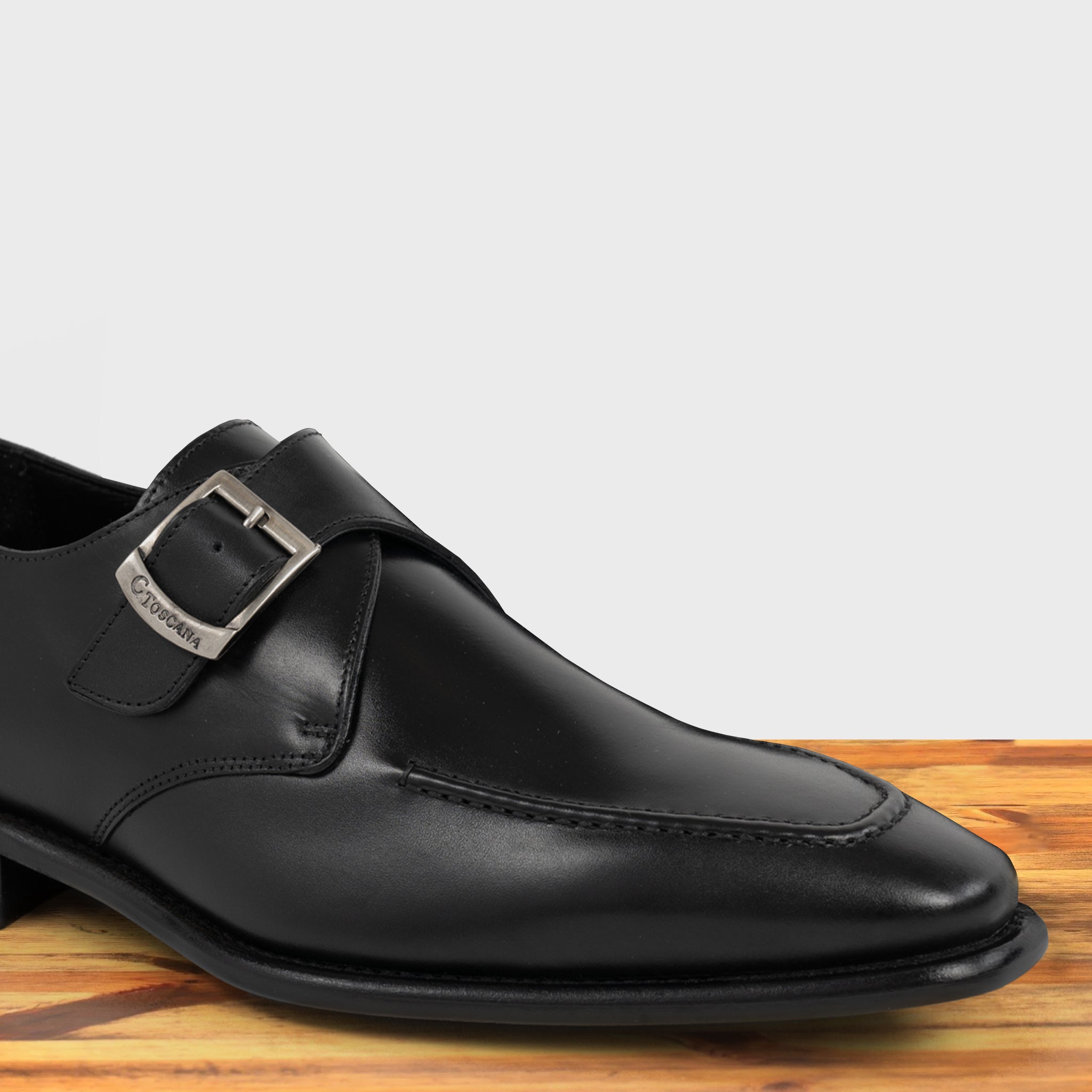 A black monk strap shoe with a silver buckle on a wooden surface