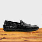 Black crocodile-patterned loafer on a wooden surface with a light gray background