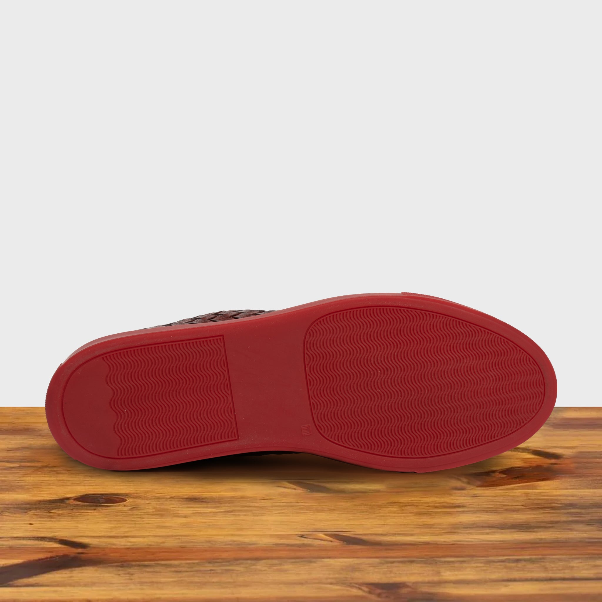 Outsole of Cherry  high-top sneaker with woven pattern on a wooden surface