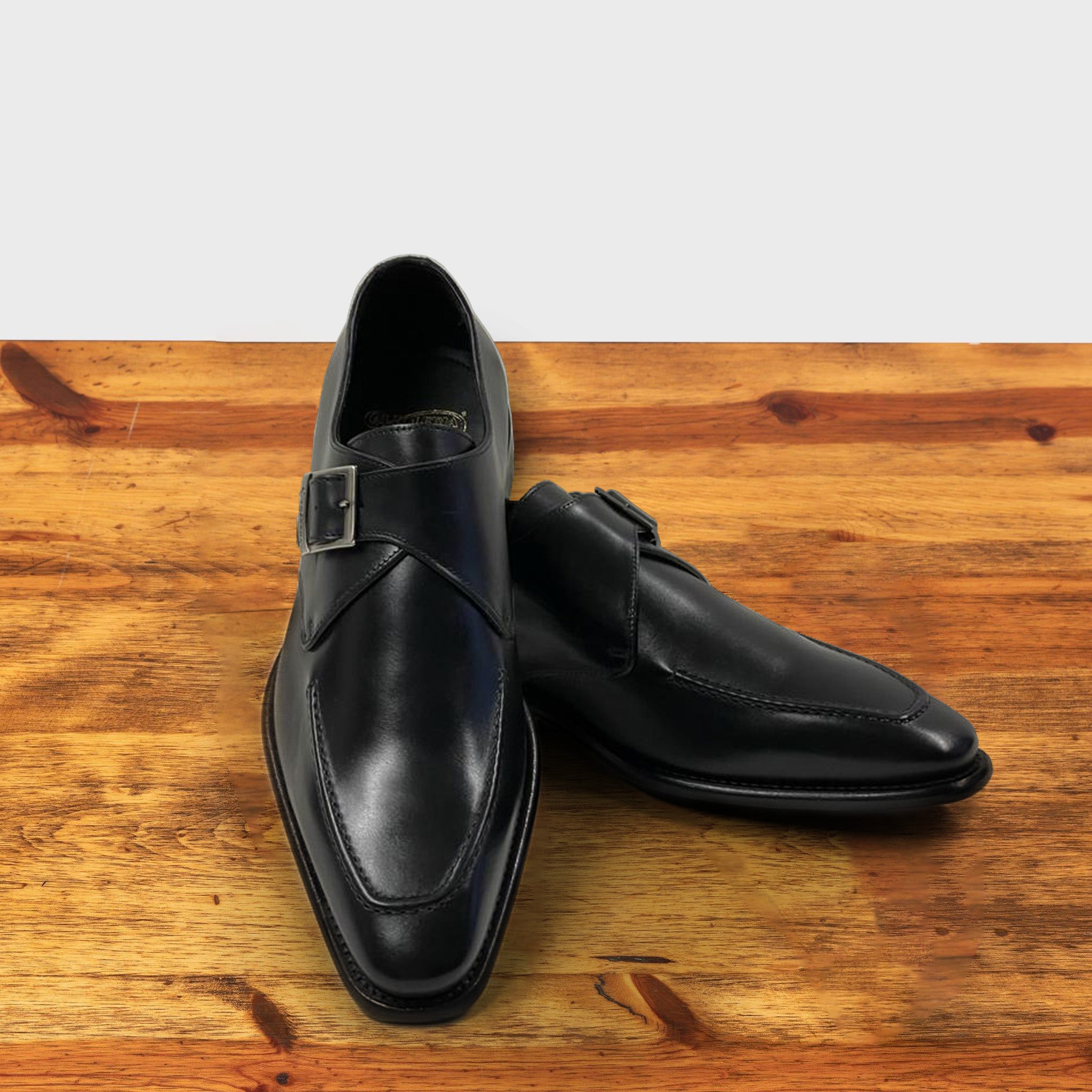 A Pair of  black monk strap shoe with a silver buckle on a wooden surface