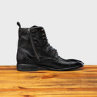 Black leather boot on a wooden surface with a light gray background