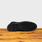 Outsole of Black leather boot on a wooden surface with a light gray background
