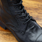 Close view of Black leather boot on a wooden surface