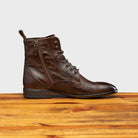 Brown leather boot on a wooden surface with a light gray background