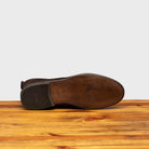 Outsole of Brown leather boot on a wooden surface with a light gray background