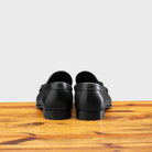Back view of black loafer shoe on a wooden surface with a light gray background
