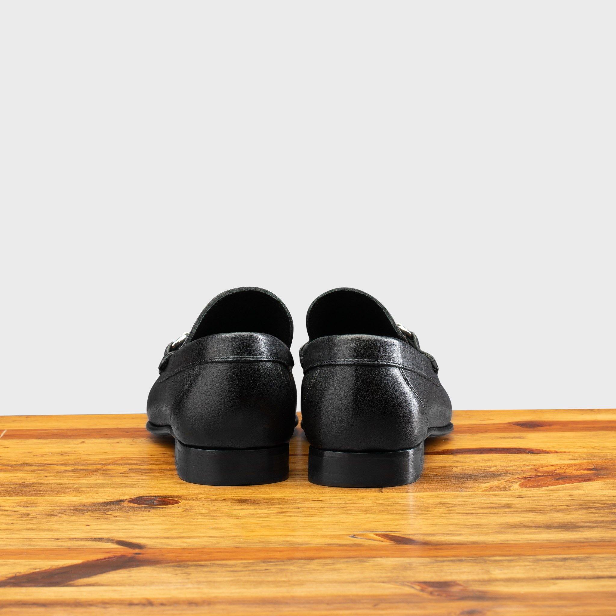 Back view of black loafer shoe on a wooden surface with a light gray background