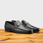 Pair of Black loafer shoe on a wooden surface with a light gray background
