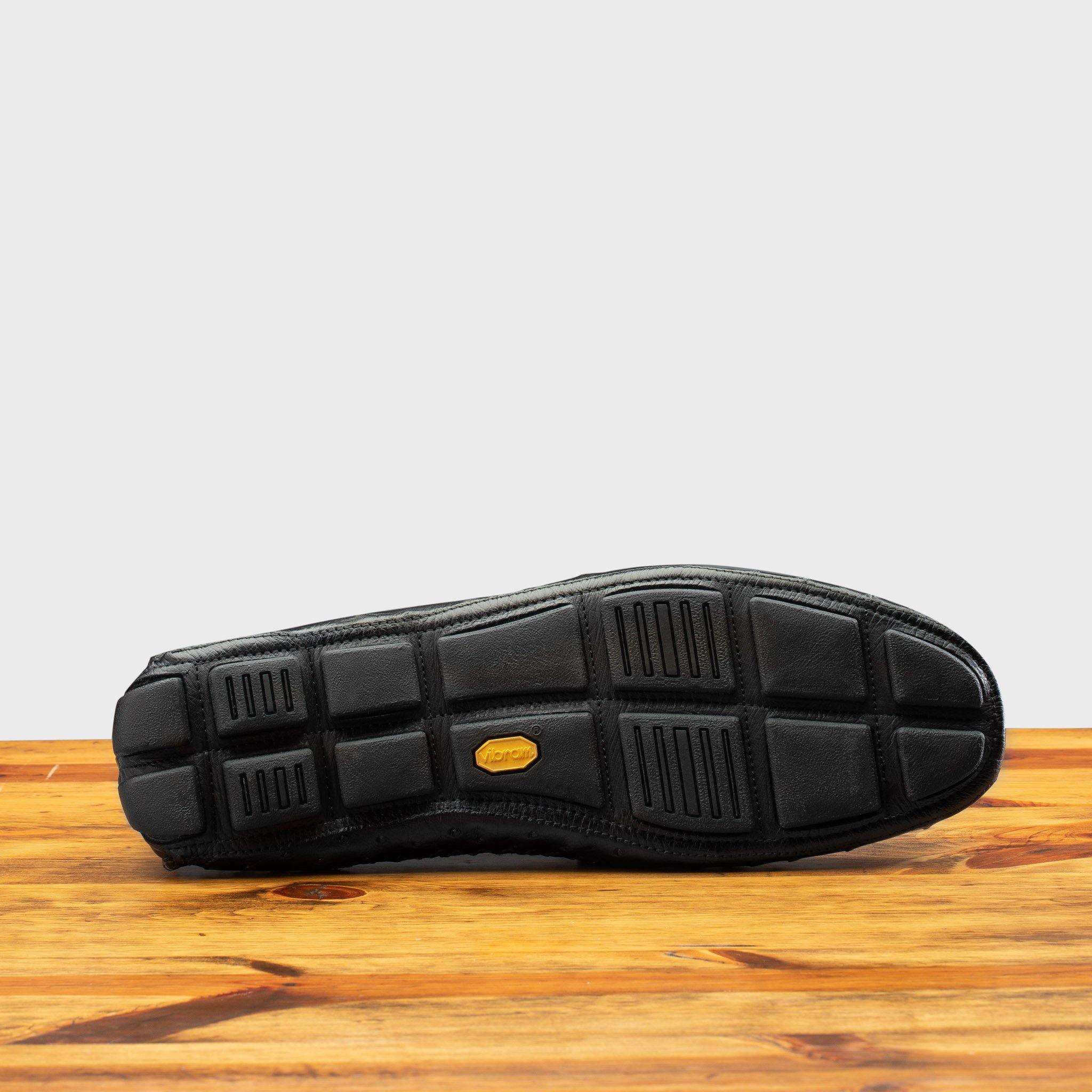 Outsole of Black leather loafer on a wooden surface with a light gray background