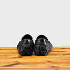 Back view of Black leather loafer on a wooden surface with a light gray background