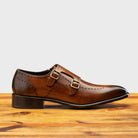 Brown leather dress shoe with gold buckle on a wooden surface
