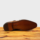 Outsole of Brown leather dress shoe with gold buckle on a wooden surface