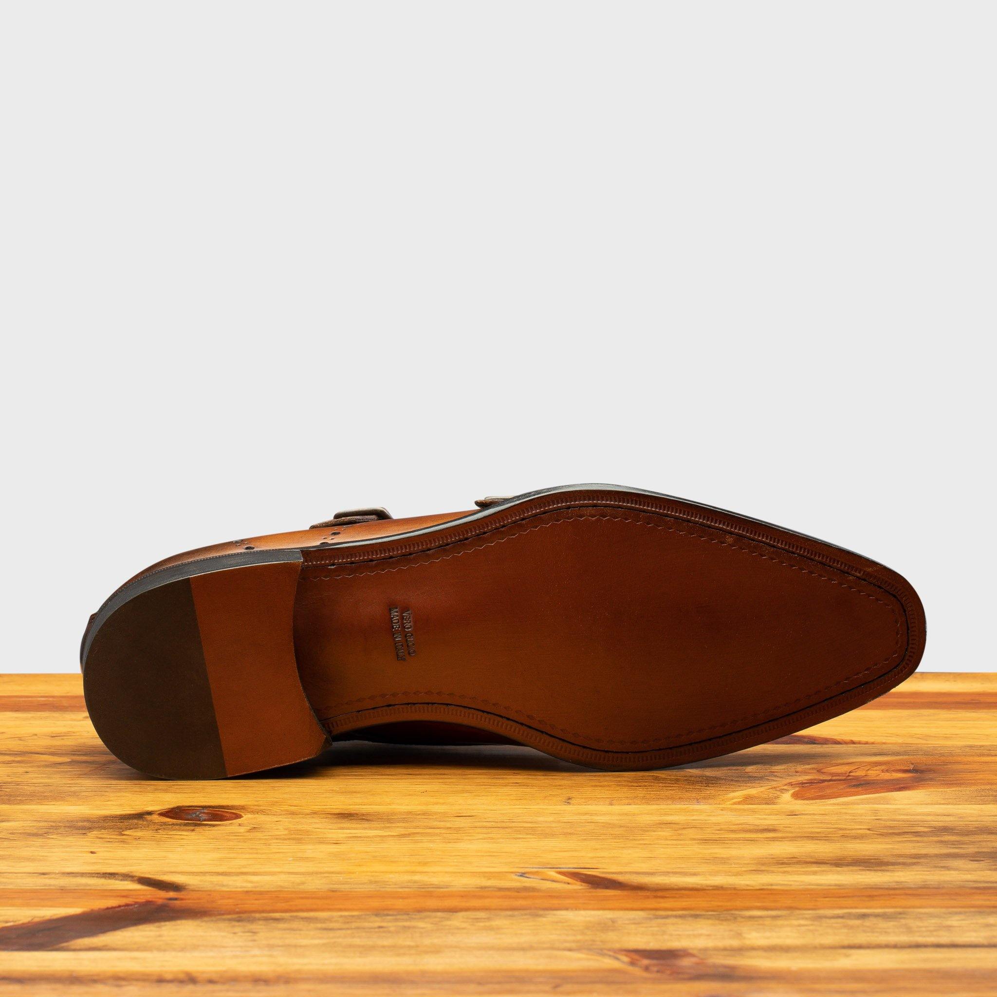 Outsole of Brown leather dress shoe with gold buckle on a wooden surface