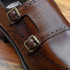 Brown leather dress shoe with gold buckle on a wooden surface