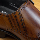 Brown leather dress shoe with gold buckle close view on a wooden surface