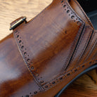 Brown leather dress shoe with gold buckle close view on a wooden surface