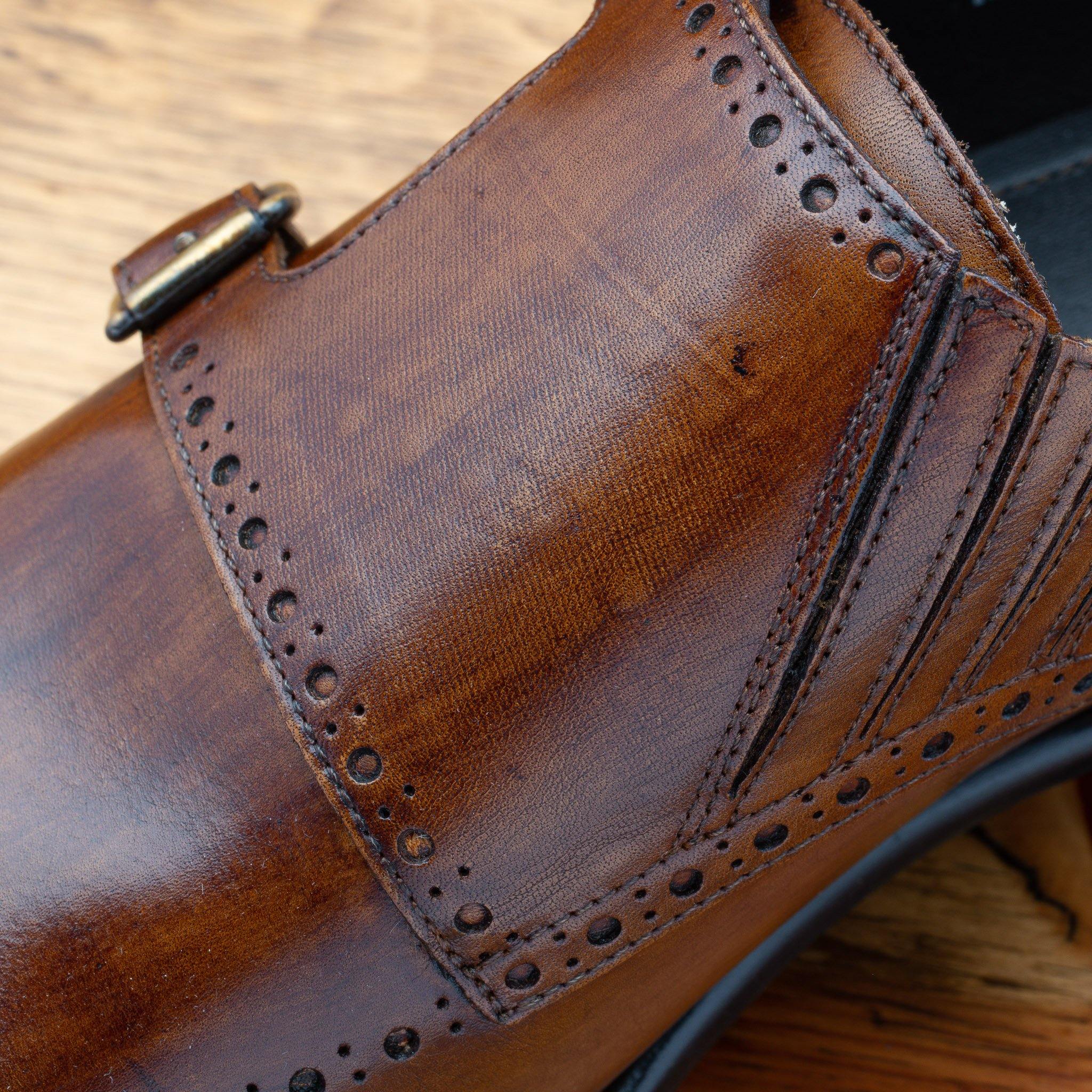 Brown leather dress shoe with gold buckle close view on a wooden surface