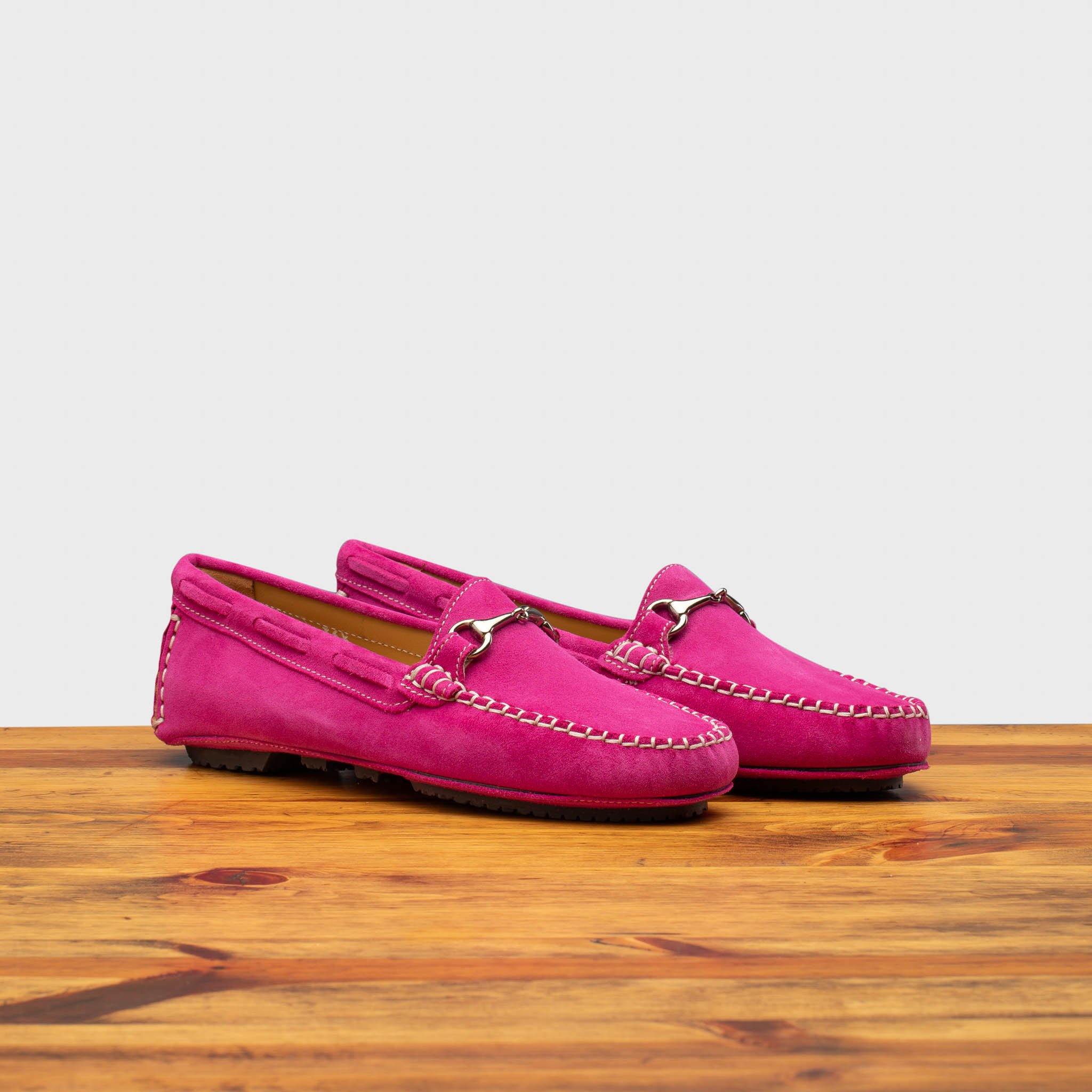 Pair of pink loafers on a wooden surface with a white background