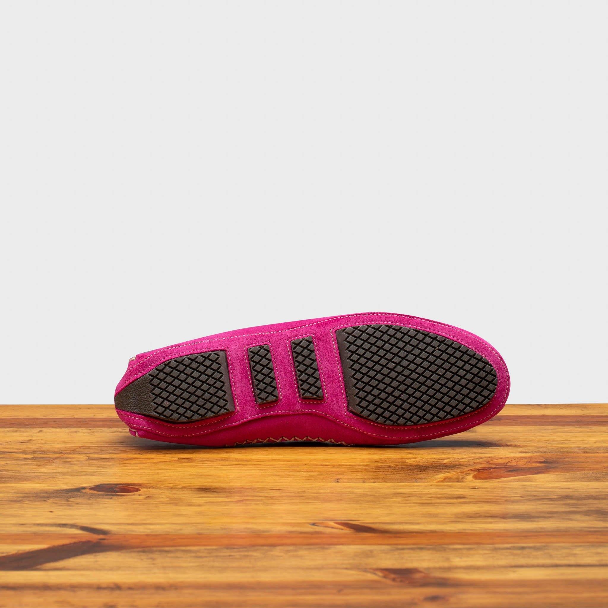 Outsole of pink loafers on a wooden surface with a white background