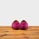 Back side of pink loafers on a wooden surface with a white background