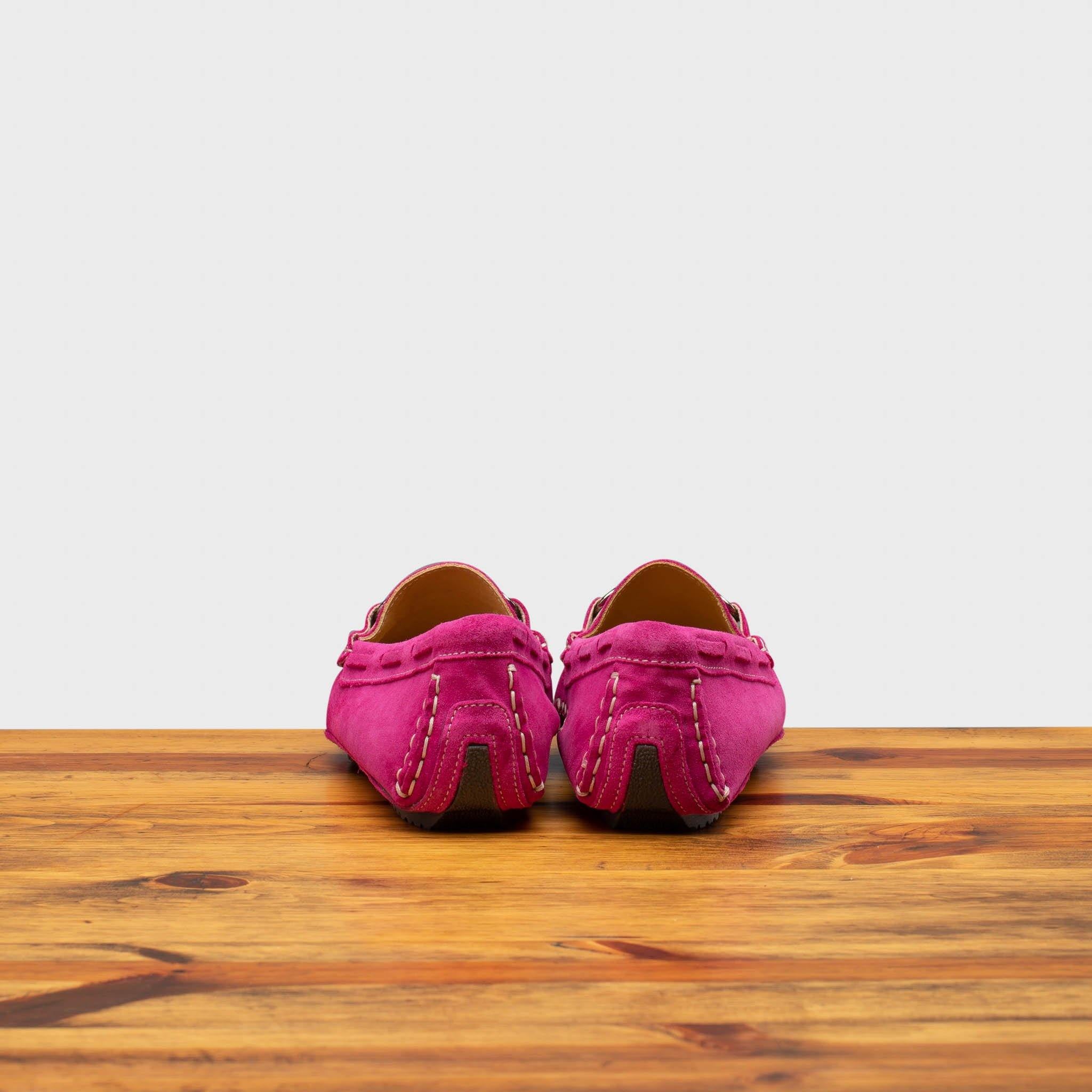 Back side of pink loafers on a wooden surface with a white background