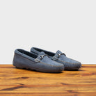 A pair of blue velour suede driver shoes with a metallic bit, placed on a wooden surface.