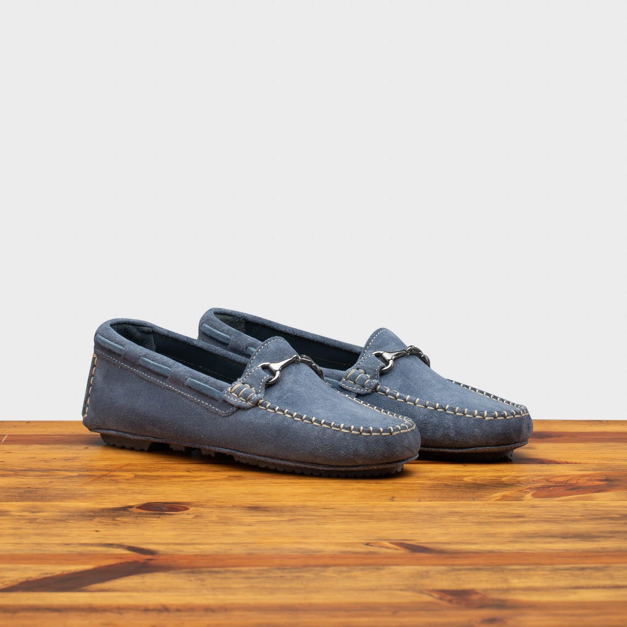 A pair of blue velour suede driver shoes with a metallic bit, placed on a wooden surface.