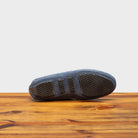 Outsole of blue velour suede driver shoes with a metallic bit, placed on a wooden surface.