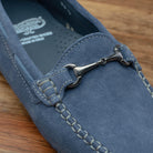 Close view of blue velour suede driver shoes with a metallic bit, placed on a wooden surface.