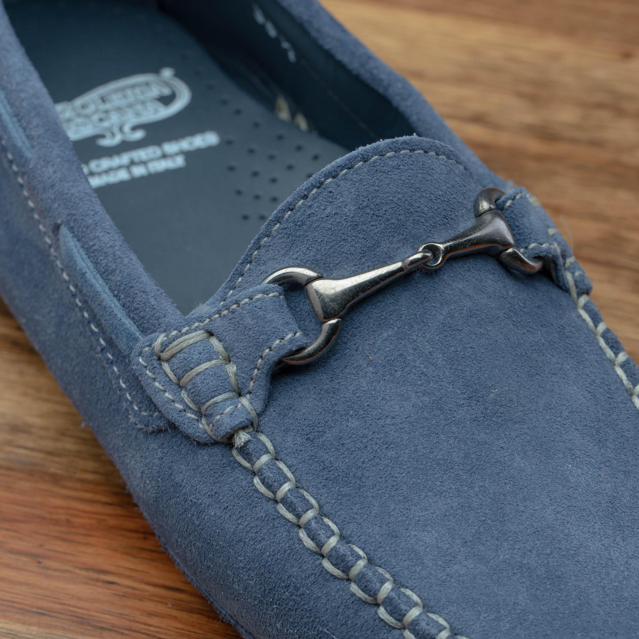Close view of blue velour suede driver shoes with a metallic bit, placed on a wooden surface.