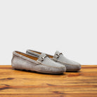 A pair of silver velour suede driver shoes with a metallic bit, placed on a wooden surface.