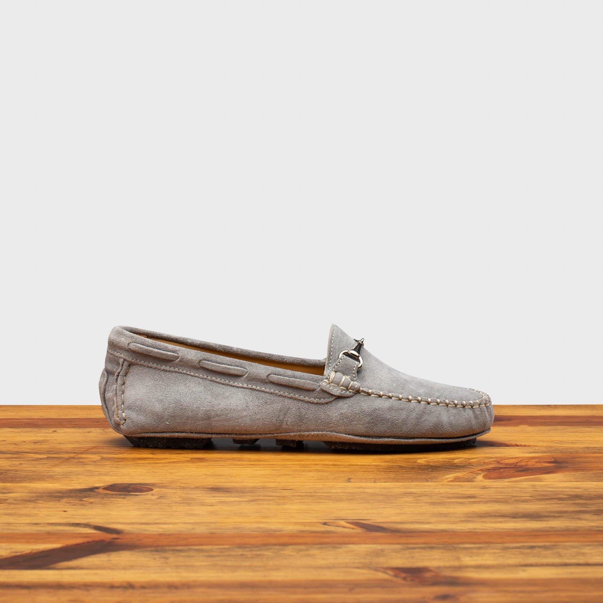 Silver velour suede driver shoes with a metallic bit, placed on a wooden surface.