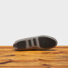 Outsole of Silver velour suede driver shoes with a metallic bit, placed on a wooden surface.