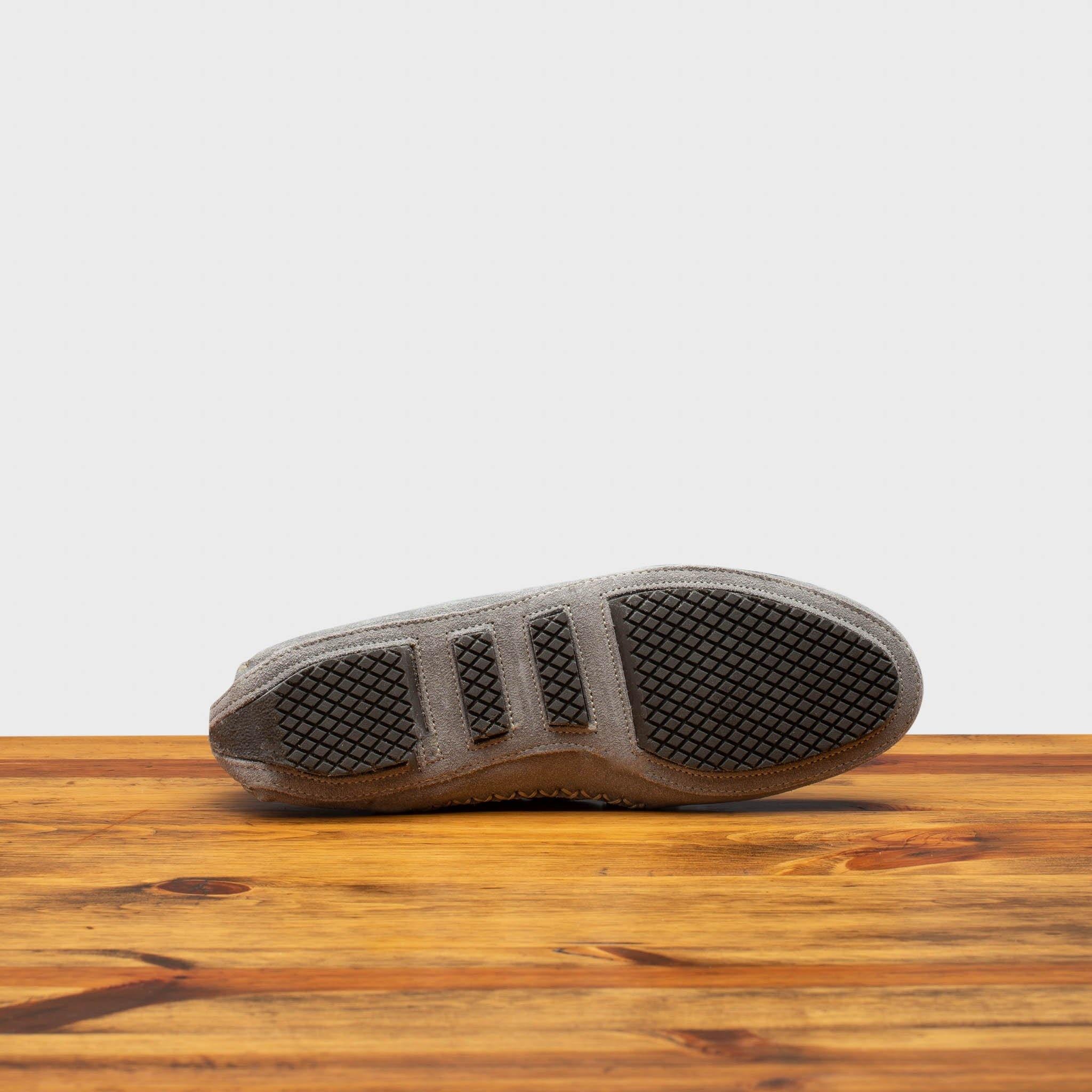 Outsole of Silver velour suede driver shoes with a metallic bit, placed on a wooden surface.
