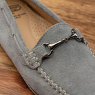Silver velour suede driver shoes with a metallic bit, placed on a wooden surface.