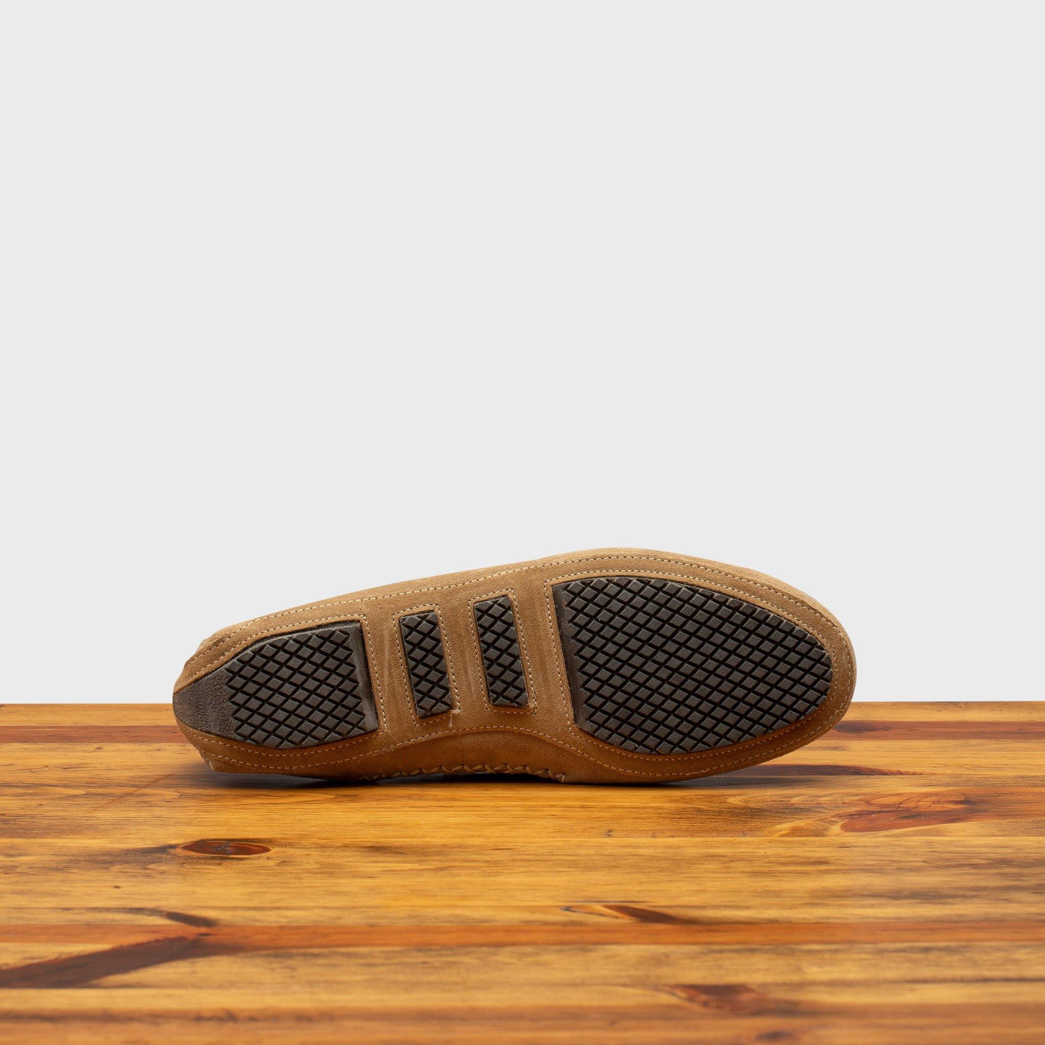 Outsole of rope velour suede driver shoes with a metallic bit, placed on a wooden surface.
