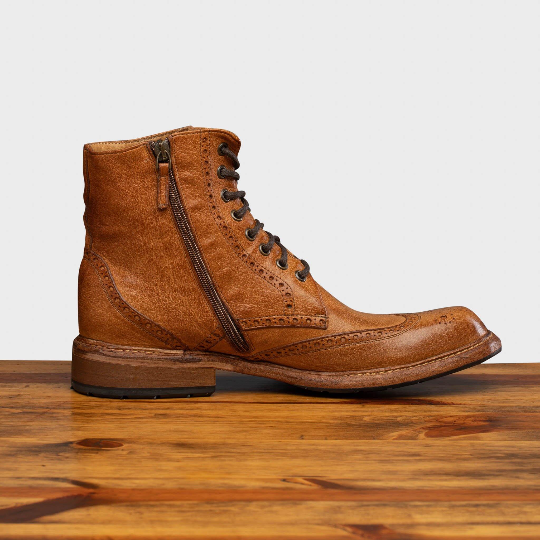 Brick pair of leather boots on a wooden surface with a light gray background