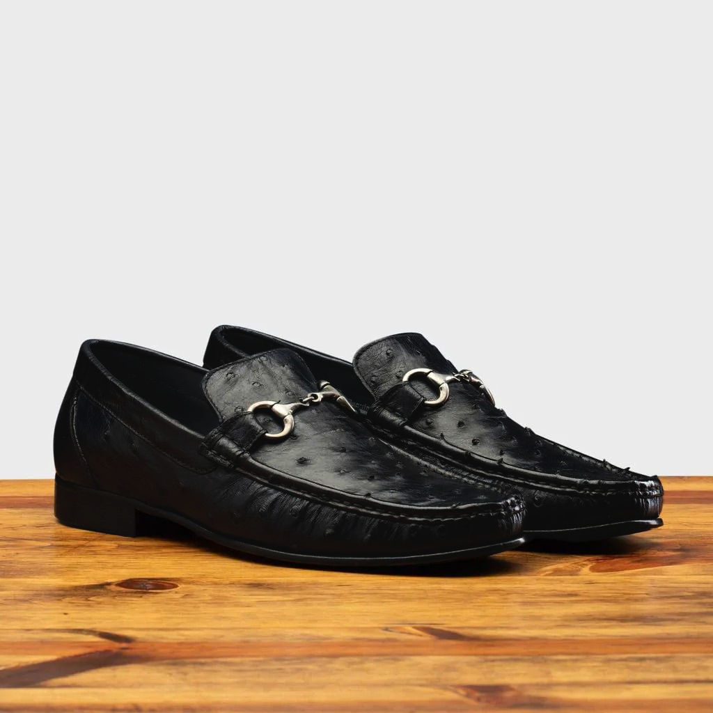 Pair of Black leather loafer on a wooden surface with a light gray background
