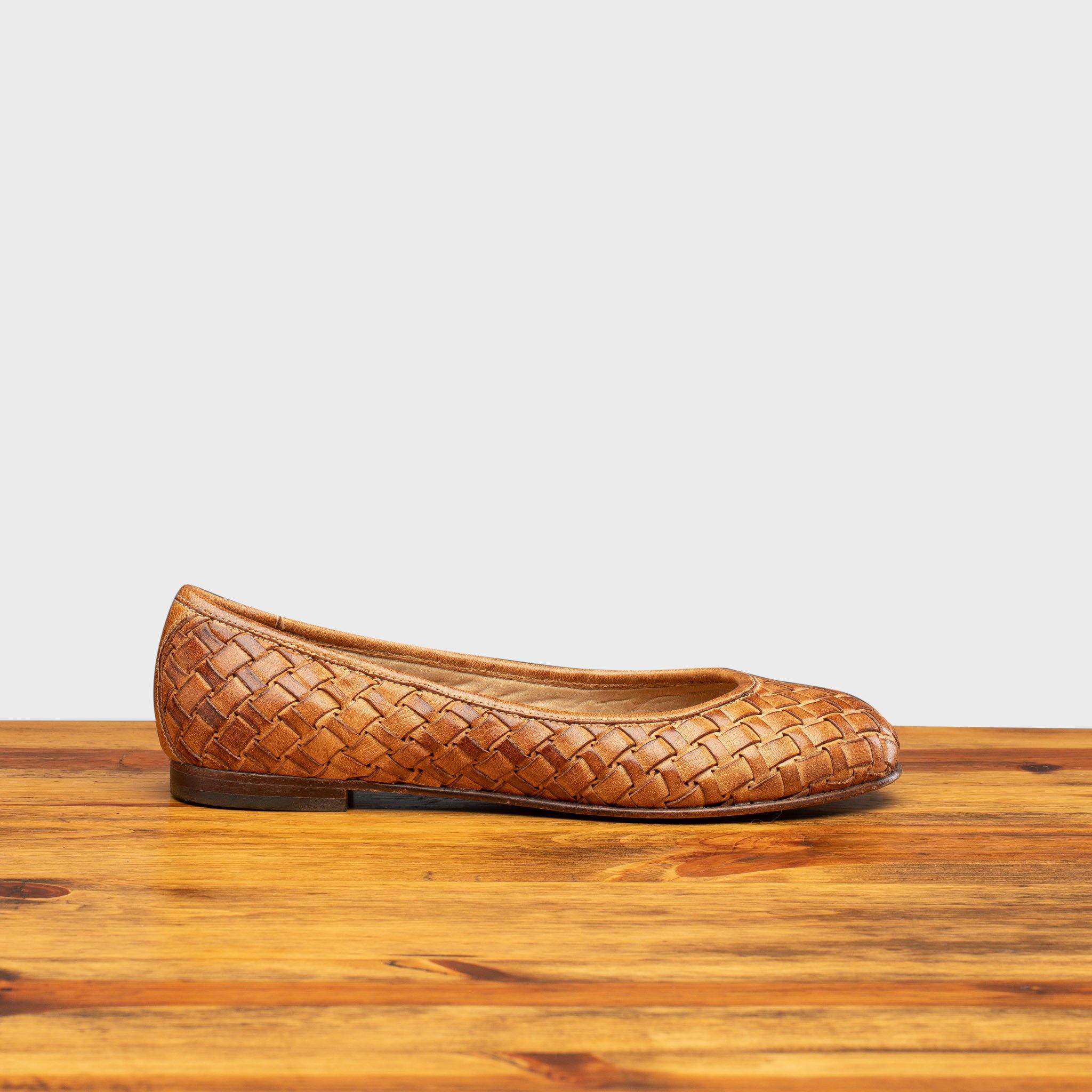 Brick woven flat shoe on a wooden surface with a light gray background