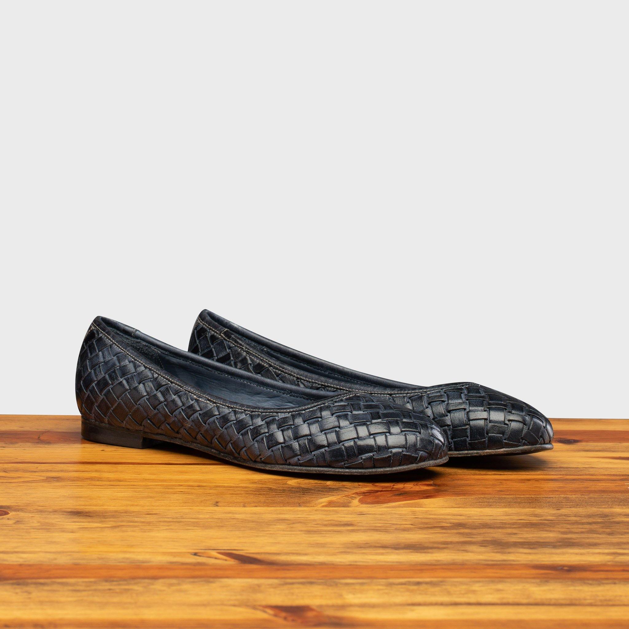 Pair of Navy Blue woven flat shoe on a wooden surface with a light gray background