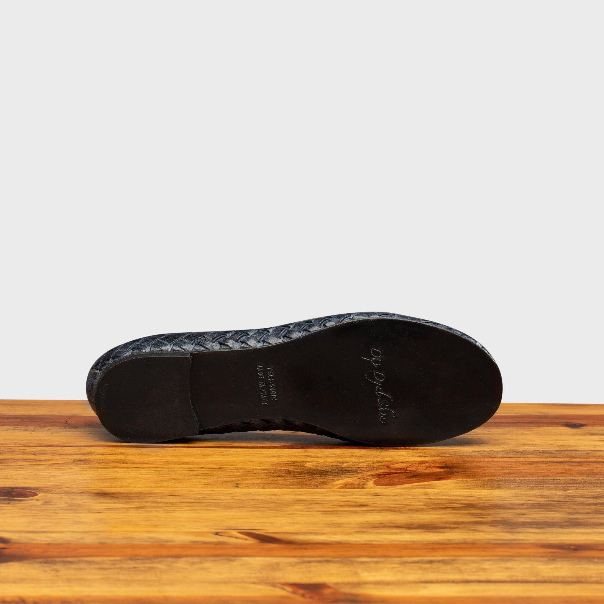Outsole of Navy Blue woven flat shoe on a wooden surface with a light gray background