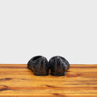 Back Side of Navy Blue woven flat shoe on a wooden surface with a light gray background