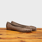 Pair of Taupe woven flat shoe on a wooden surface with a light gray background