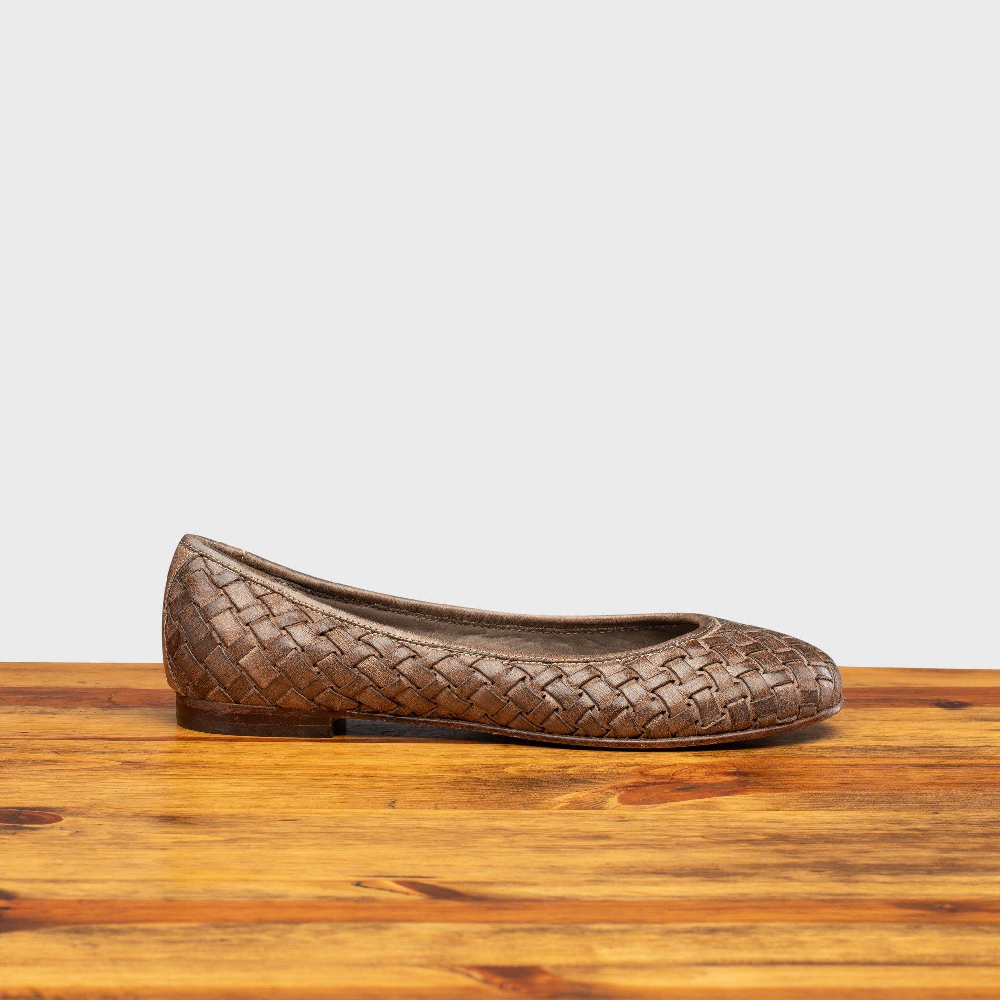 Taupe woven flat shoe on a wooden surface with a light gray background